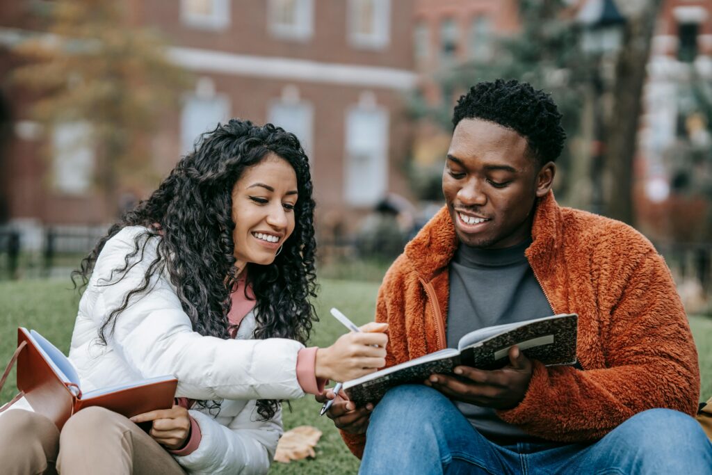 Male and female student Holding Notebooks While Sitting on Grass