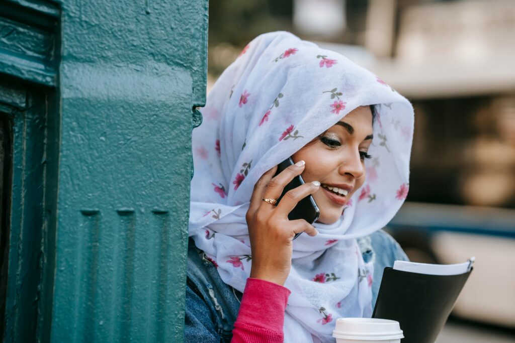 Smiling female student talking via modern smartphone in city street