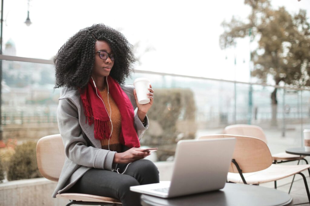 A university female student sitting outside and taking a coffee while working on her laptop