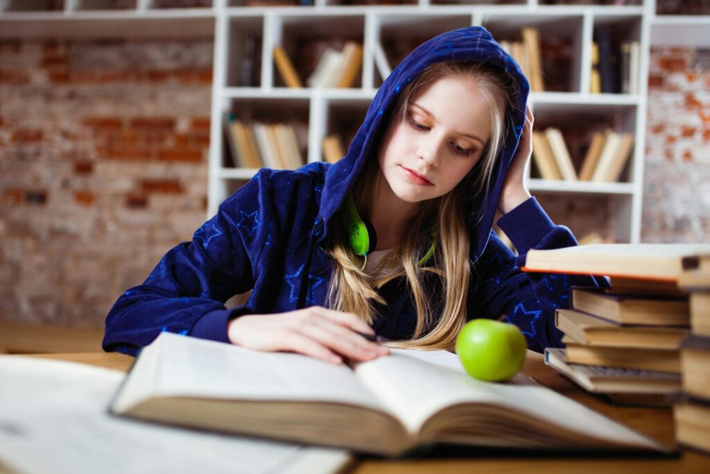 Picture of a woman wearing blue jacket sitting on chair near table reading books